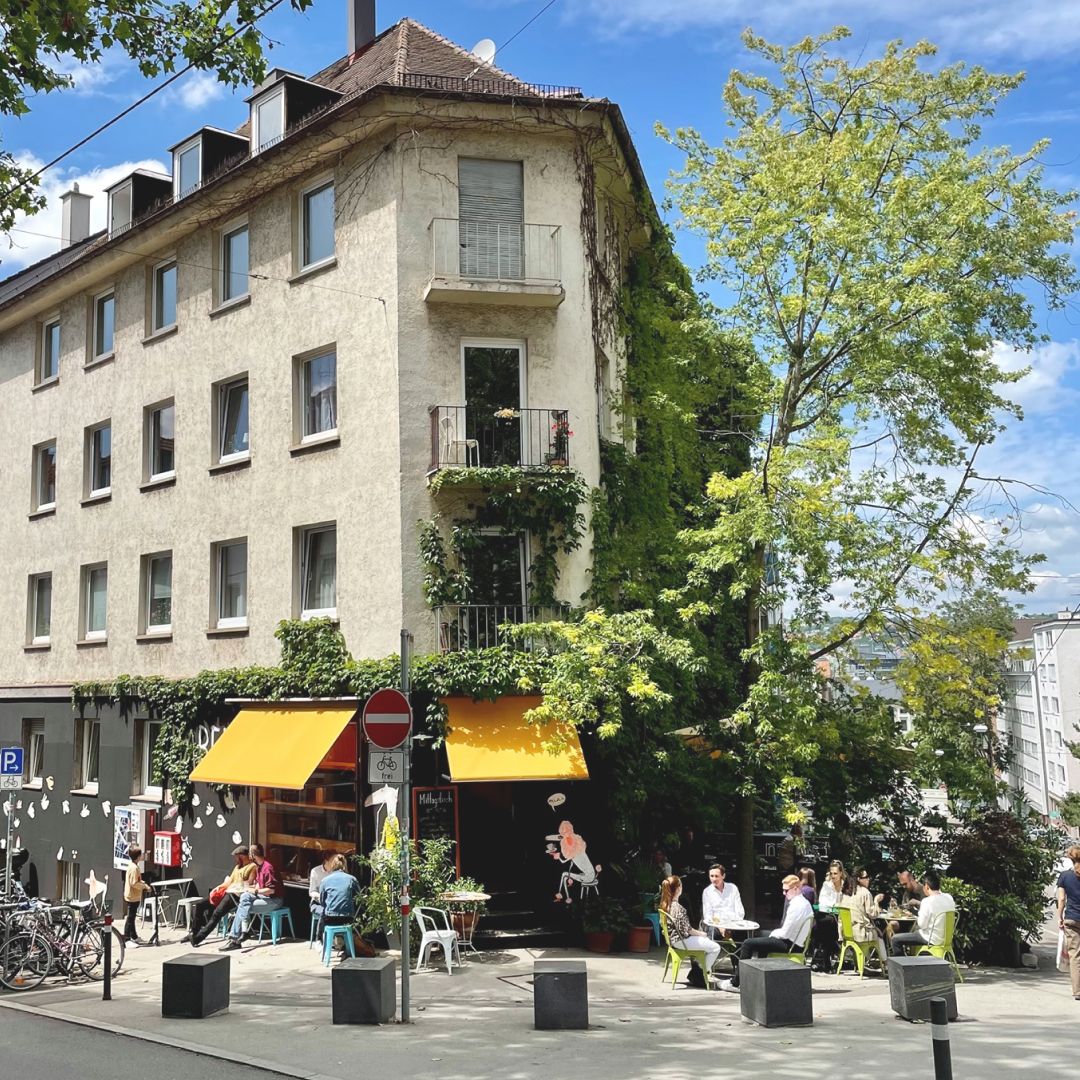 Das Café Moody von außen mit Efeu, gelben Markisen und Stühlen auf dem Gehweg